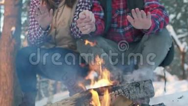 一对年轻人穿着冬天的衣服在树林里，温<strong>暖</strong>他们的手在火边，一次<strong>冬季</strong>野餐